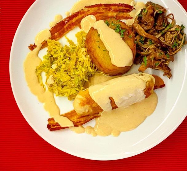 Image with a dish with Corn fed chicken breast, served with potatoes fondant, savoy cabbage, and a pancetta sauce.